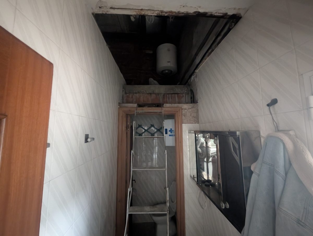 Empresas de reformas en Burgos - Reformas de baños, cocinas y tejados Zona de servicio al fondo de un local en Burgos con el falso techo abierto y un termo eléctrico